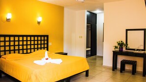 Une chambre d’hôtel comprenant un lit, une table de chevet, une commode et un bureau avec un miroir et une plante.