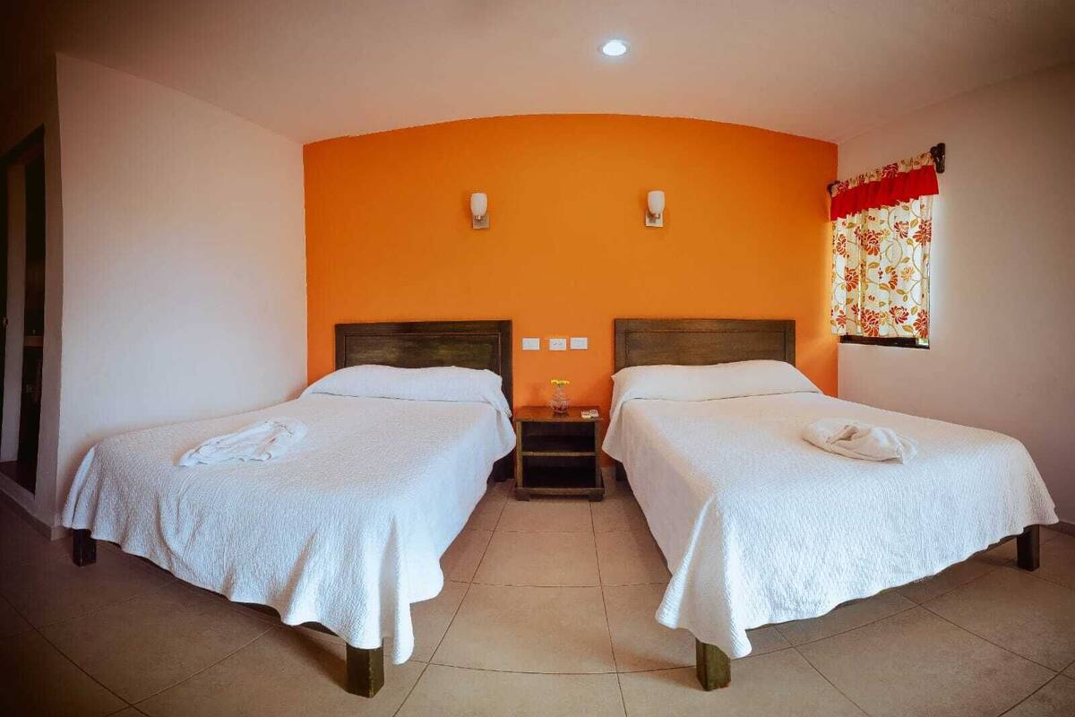 A room with two beds, a nightstand, a wall-mounted light, and a window with curtains.