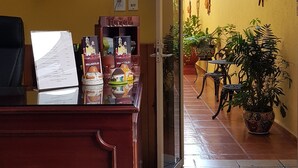 Un espace d’accueil d’hôtel avec un comptoir en bois, des certificats encadrés, une horloge et un panneau indiquant qu’il est interdit d’y introduire des animaux de compagnie.