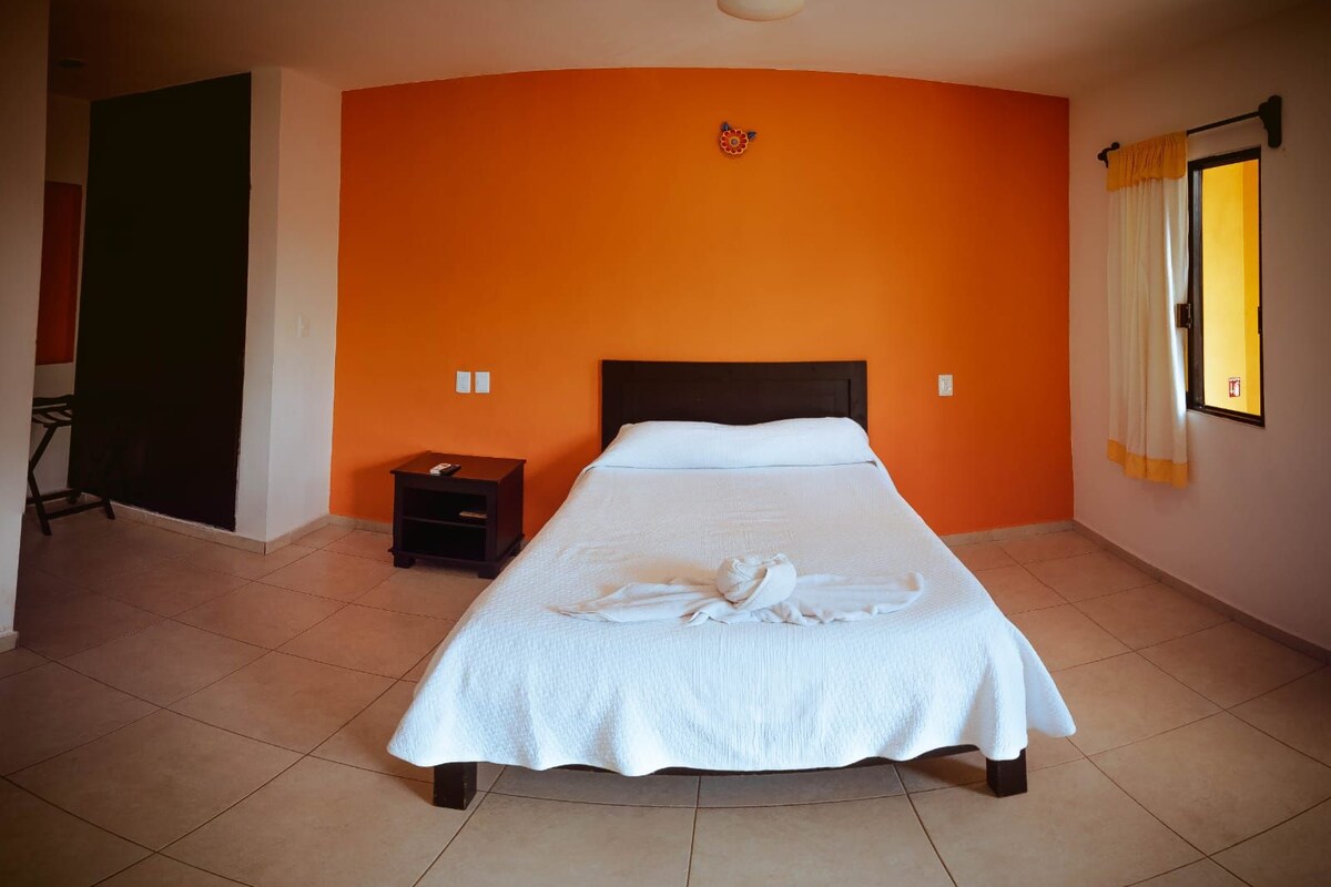A hotel room with a bed, a nightstand, a wall clock, and a window with curtains.