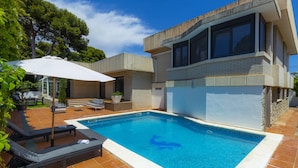 A modern house with a swimming pool, outdoor furniture, and a large umbrella.