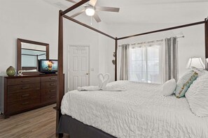 Un dormitorio con una cama con dosel, un ventilador de techo, un televisor sobre un aparador y una puerta decorada con corazones.