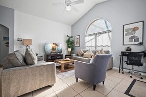 A spacious living room with a high ceiling, a television, a coffee table, and a comfortable seating area.