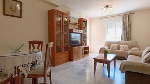A living room with a glass dining table, wooden chairs, a sofa, a TV, and a cabinet. - TERRASOL AZUCARERA 3 DORMITORIOS (Torre del Mar)