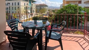 A balcony with a table and chairs, overlooking a cityscape with buildings and mountains. - TERRASOL AZUCARERA 3 DORMITORIOS (Torre del Mar)