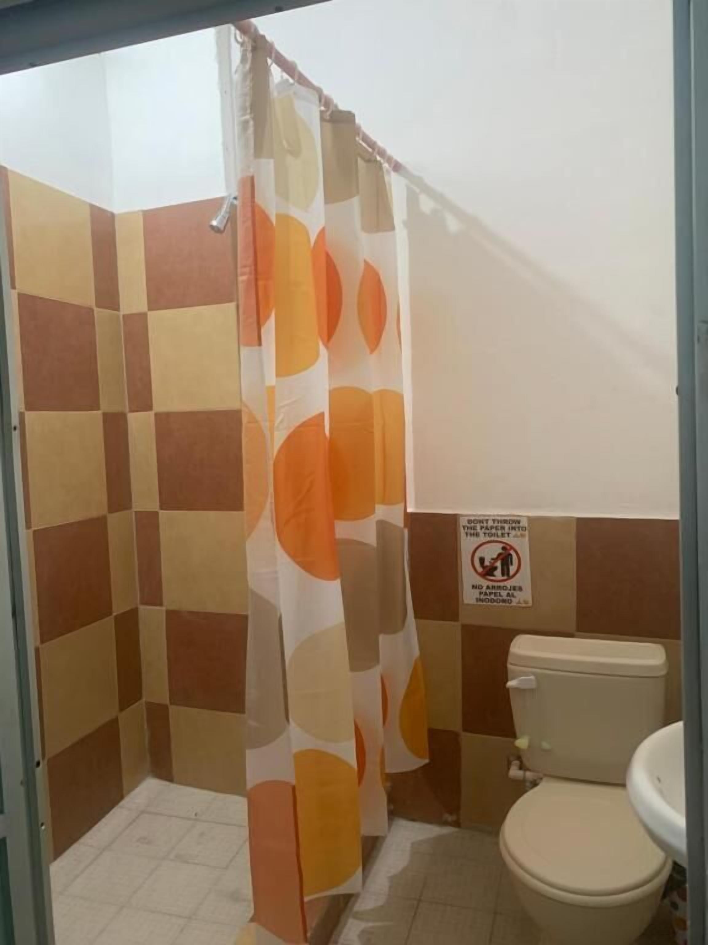 Une salle de bain avec un rideau de douche orné de cercles orange et blancs, des toilettes et un panneau interdisant de jeter du papier dans les toilettes.