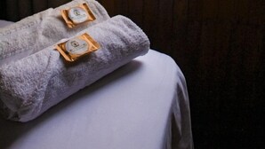 Une pièce avec un mur lambrissé en bois, une fenêtre donnant sur un paysage verdoyant et un lit recouvert d’un drap blanc, ainsi que deux serviettes ornées d’un logo.