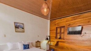 Une chambre avec un plafond en bois, un lit avec une literie blanche, un tableau accroché au mur et un téléviseur fixé au mur en bois.
