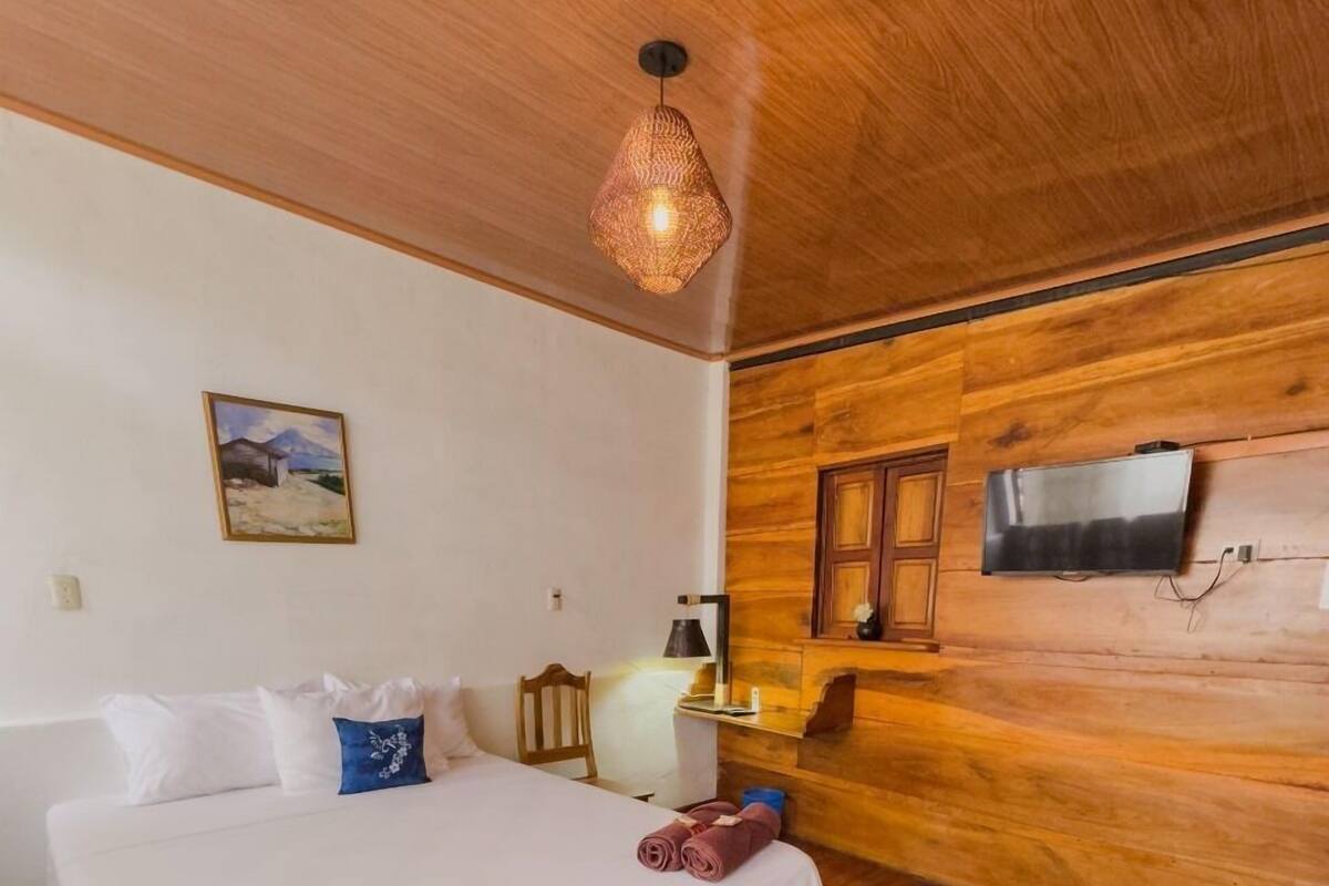 Une chambre avec un plafond en bois, un lit avec une literie blanche, un tableau accroché au mur et un téléviseur fixé au mur en bois.