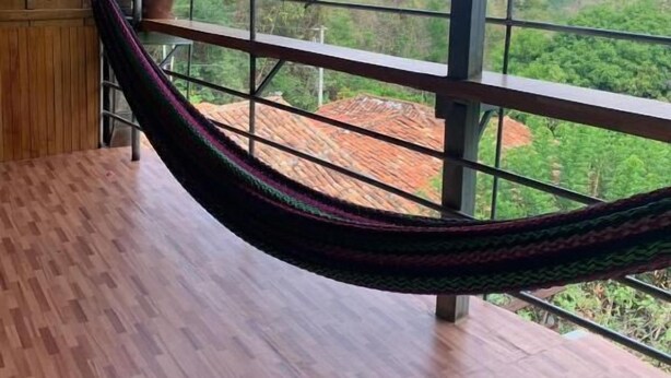 Un hamac sur un balcon, avec vue sur un paysage luxuriant et une chaîne de montagnes lointaine.
