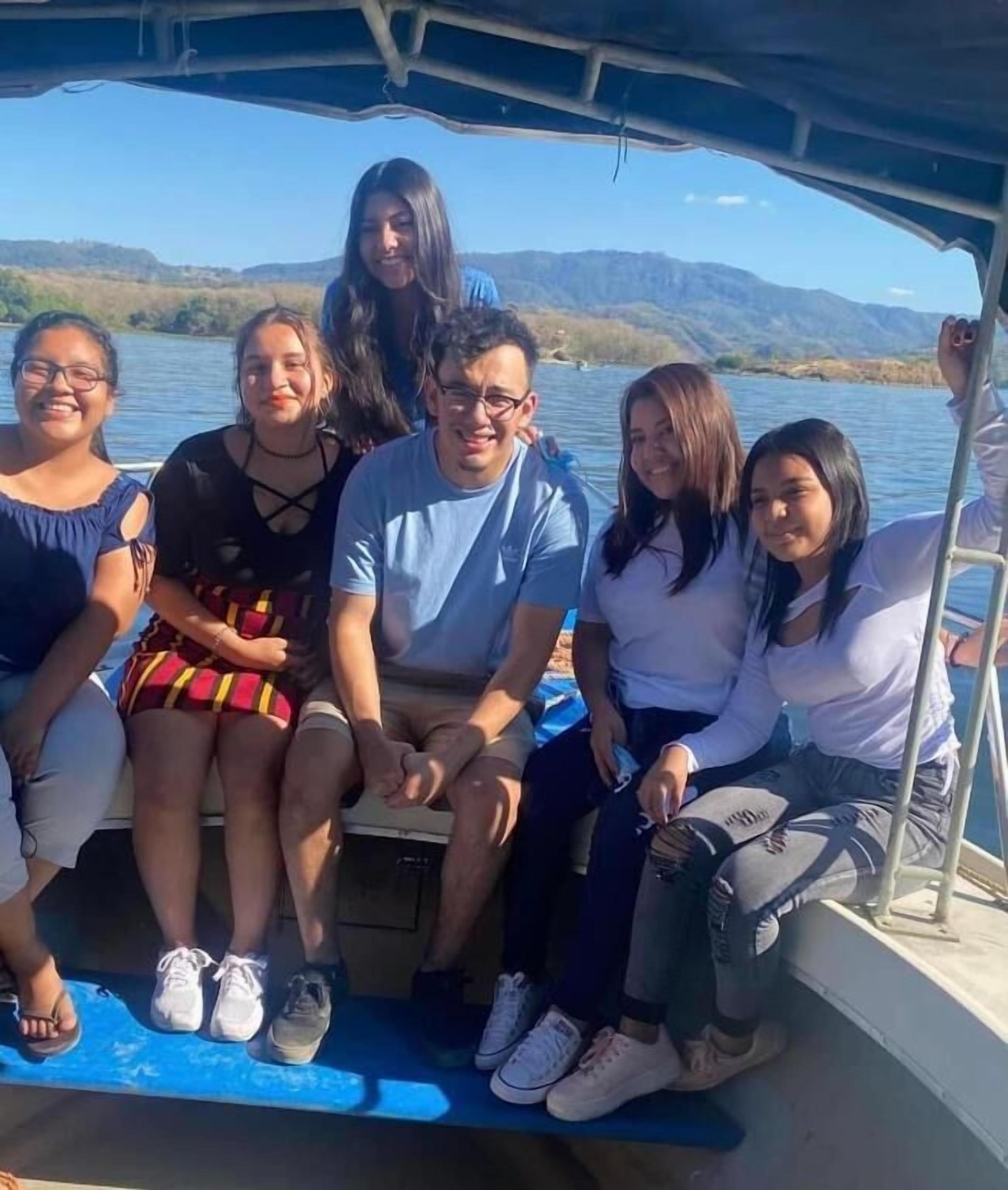Un groupe de personnes se trouve sur un bateau, avec une vue sur un lac et des montagnes en arrière-plan.