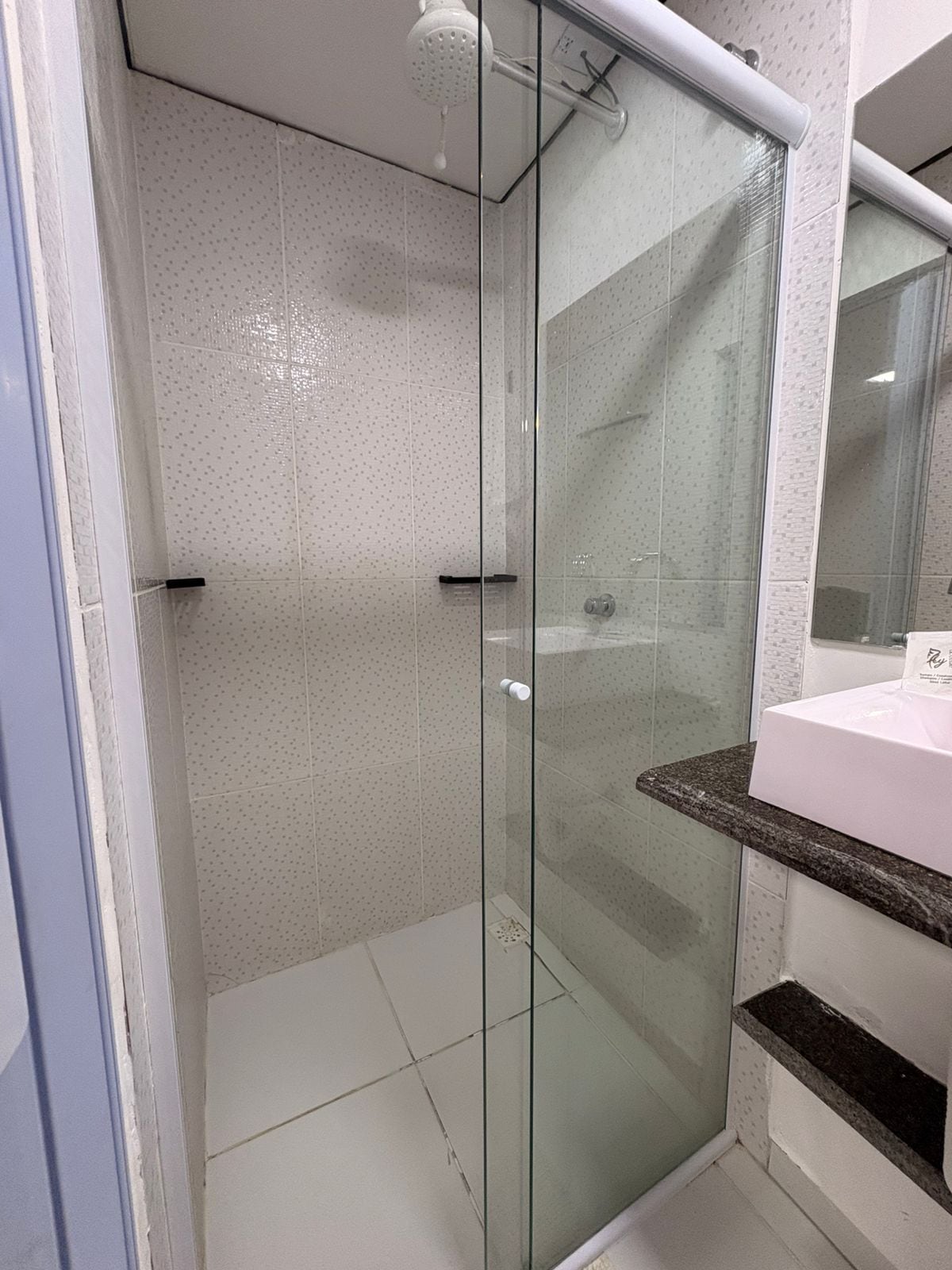 Un box de ducha con paredes de vidrio, pared de azulejos blancos y una encimera de mármol a su lado.