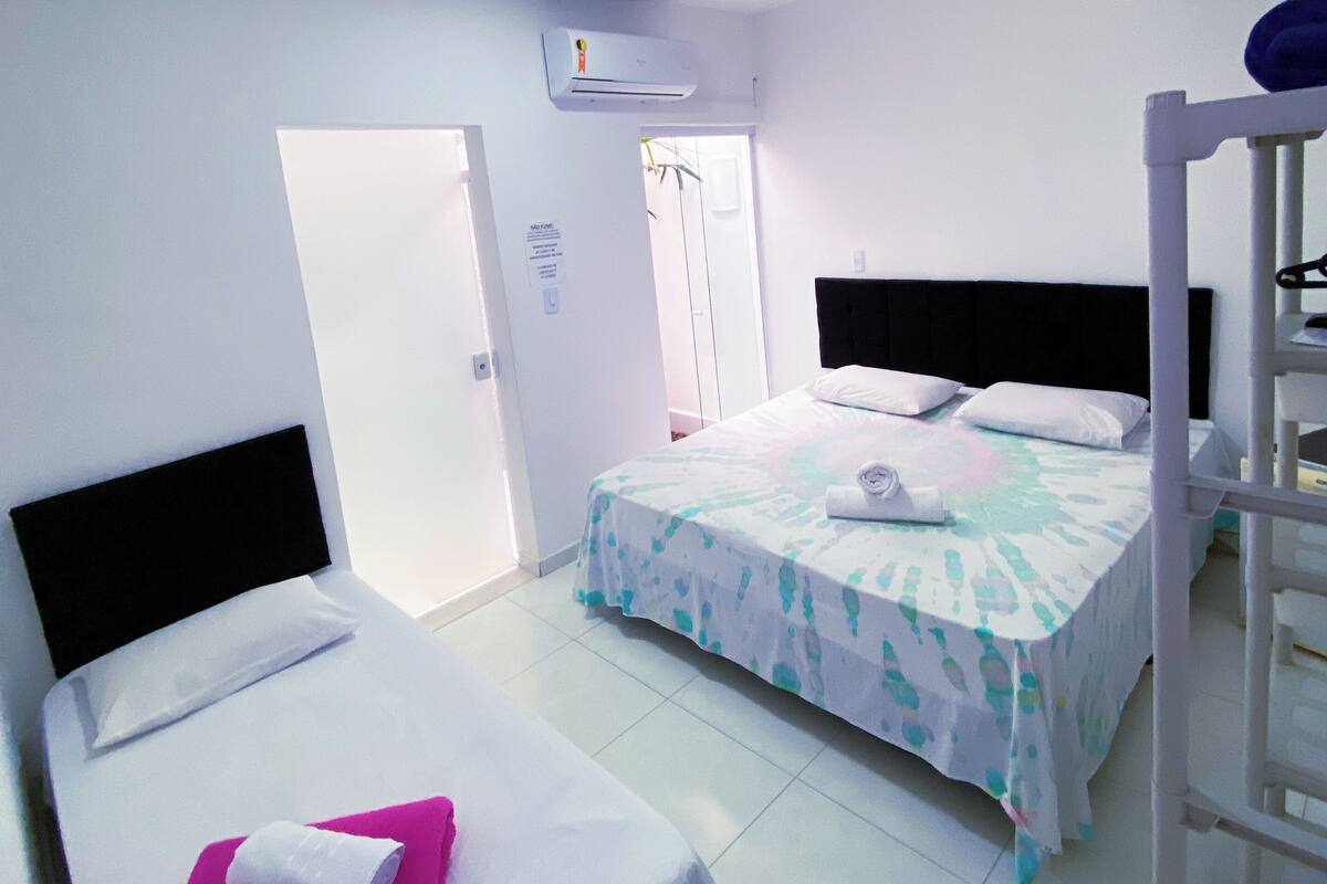 A hotel room with two beds, a bunk bed, a white air conditioner, and a door leading to another room.