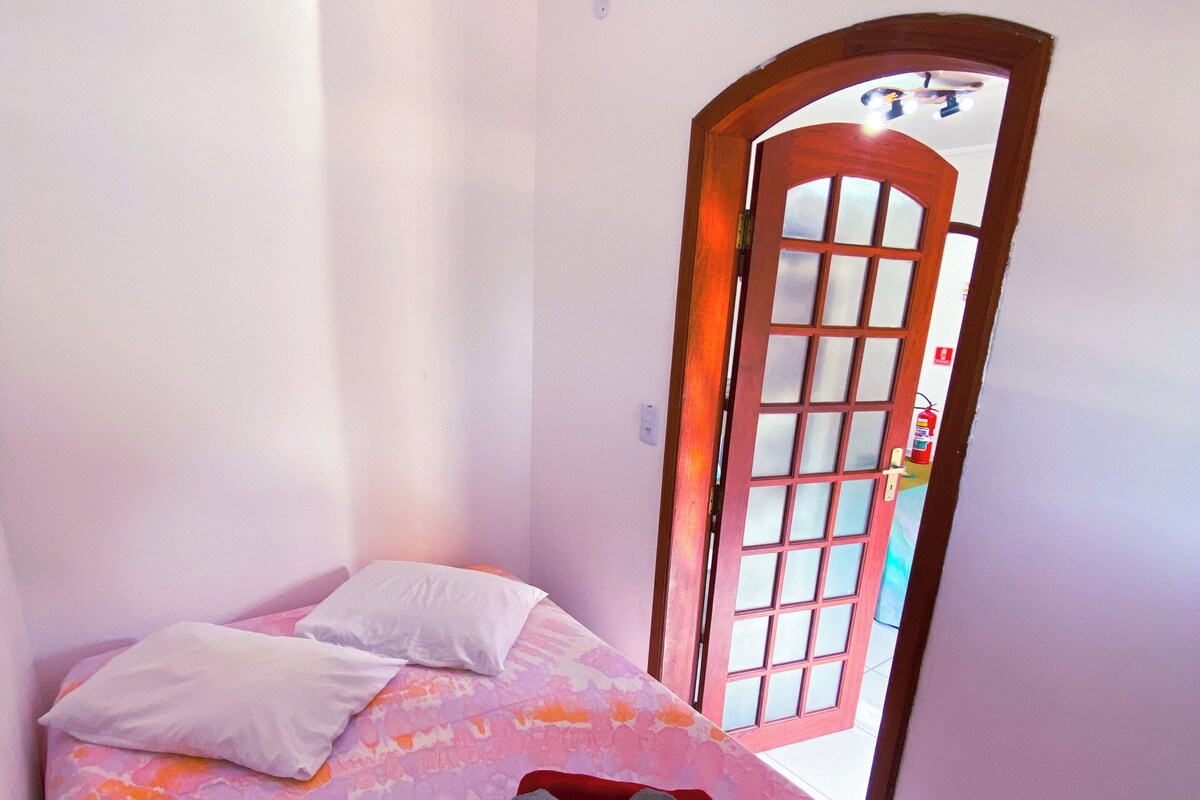 Una cama individual con una colcha de colores, una almohada blanca y una toalla enrollada encima.