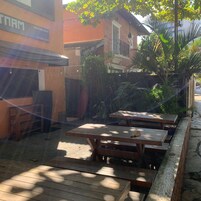 Un espacio al aire libre con patio, mesas y bancos de madera, rodeado de follaje y un edificio de ladrillo.