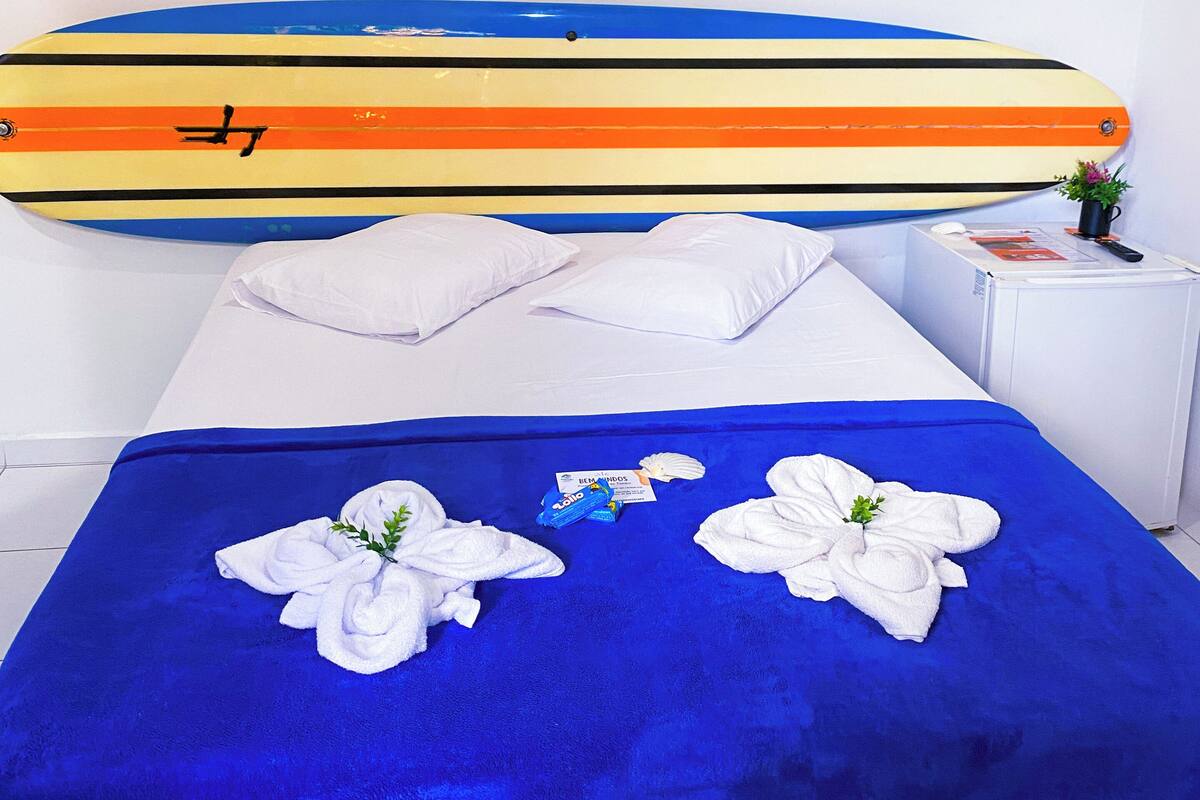 A hotel room with a bed, a surfboard, and a logo on the wall.