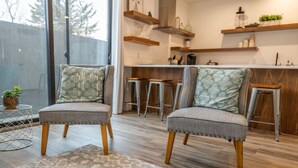 Una cocina moderna con suelo de madera, dos taburetes de bar y una zona de comedor con un rug adornado.