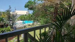 A balcony with a view of a swimming pool, surrounded by lush greenery and a building in the background. - T2 de Charme, Résidence Avec Piscine à 500m de la Plage du Diamant (Le Diamant)
