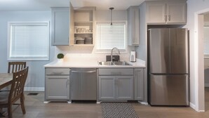 A modern kitchen with grey cabinets, a stainless steel refrigerator, and a built-in dishwasher. - Falling Prices for a Fall Getaway to Tulsa! Updated Home in Mid Tulsa. (Tulsa)