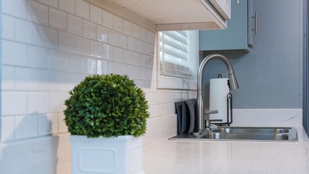 A modern kitchen with white tiles, a stainless steel sink, a faucet, and a potted plant. - Falling Prices for a Fall Getaway to Tulsa! Updated Home in Mid Tulsa. (Tulsa)