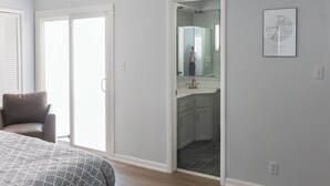 A bedroom with a bed, a chair, a bathroom with a sink and mirror, and a framed map on the wall. - Falling Prices for a Fall Getaway to Tulsa! Updated Home in Mid Tulsa. (Tulsa)