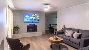 A living room with a fireplace, a sofa, a coffee table, and a TV mounted on the wall. - Falling Prices for a Fall Getaway to Tulsa! Updated Home in Mid Tulsa. (Tulsa)