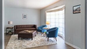 A living room with a brown sofa, blue armchairs, a coffee table, and a large window with blinds. - Falling Prices for a Fall Getaway to Tulsa! Updated Home in Mid Tulsa. (Tulsa)