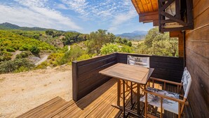 Una terraza de madera con una mesa y sillas, con vistas a un paisaje pintoresco con colinas y un río.