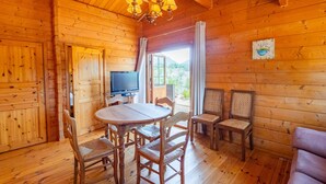 Interior de una cabaña de madera con una mesa de comedor, sillas, un televisor y un sofá.