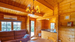 Interior acogedor de una cabaña, con paredes de madera, una mesa redonda de comedor, un sofá y una lámpara de araña.