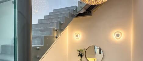 A modern interior with a glass staircase, a round mirror, and a teal chair.