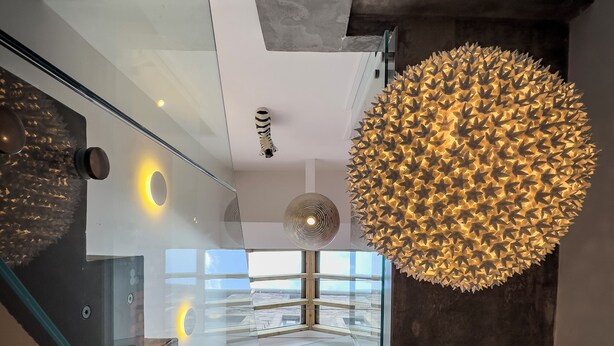 Un interior moderno con una escalera de cristal, una lámpara esférica original y vistas al exterior.