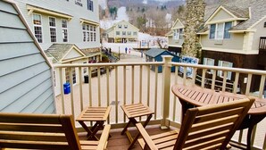 Ein Balkon mit Holzmöbeln, der auf ein Dorf mit Häusern und einem Berg im Hintergrund blickt.