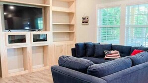 A living room with a dark blue sofa, wooden shelving, a flat-screen TV, and a ceiling fan. - Lakeview Oasis (Nevada)