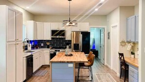 A modern kitchen with white cabinets, a central island with stools, a stainless steel refrigerator, and a built-in oven. - Lakeview Oasis (Nevada)