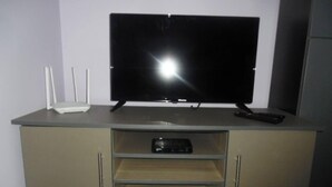 A flat-screen TV on a cabinet with a shelf below. - Travelnest Tranquility Tiny Home (Johannesburg)