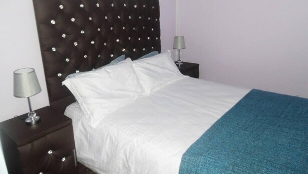 A neatly made bed with white linens and a teal throw blanket, flanked by two bedside tables with lamps, in a room with a tufted headboard and decorative wall mirrors. - Travelnest Tranquility Tiny Home (Johannesburg)