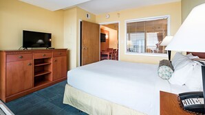 Une chambre d’hôtel équipée d’un lit, d’un bureau, d’une télévision, d’une armoire et d’une fenêtre avec des stores.