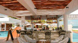 Zona de bar junto a la piscina con sillones de descanso y sombrillas, con vistas a la piscina y al océano.
