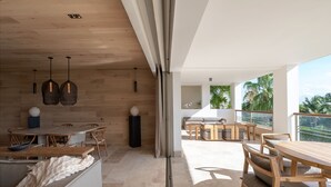 Un interior moderno con muebles de madera, un comedor y un balcón con vistas a palmeras.