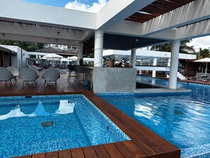 A pool area with wooden decking, lounge chairs, and umbrellas.