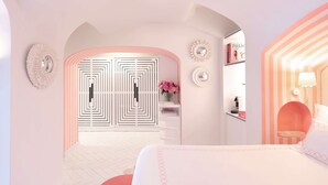 A modern bedroom with a white and pink color scheme, featuring a large bed, a vanity with a mirror, and a door with a geometric pattern. - Villa Sabrina by Elite Villas (Capri)