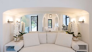 A modern, curved sofa with a white and beige color scheme, flanked by two side tables with books and decorative items. - Villa Sabrina by Elite Villas (Capri)