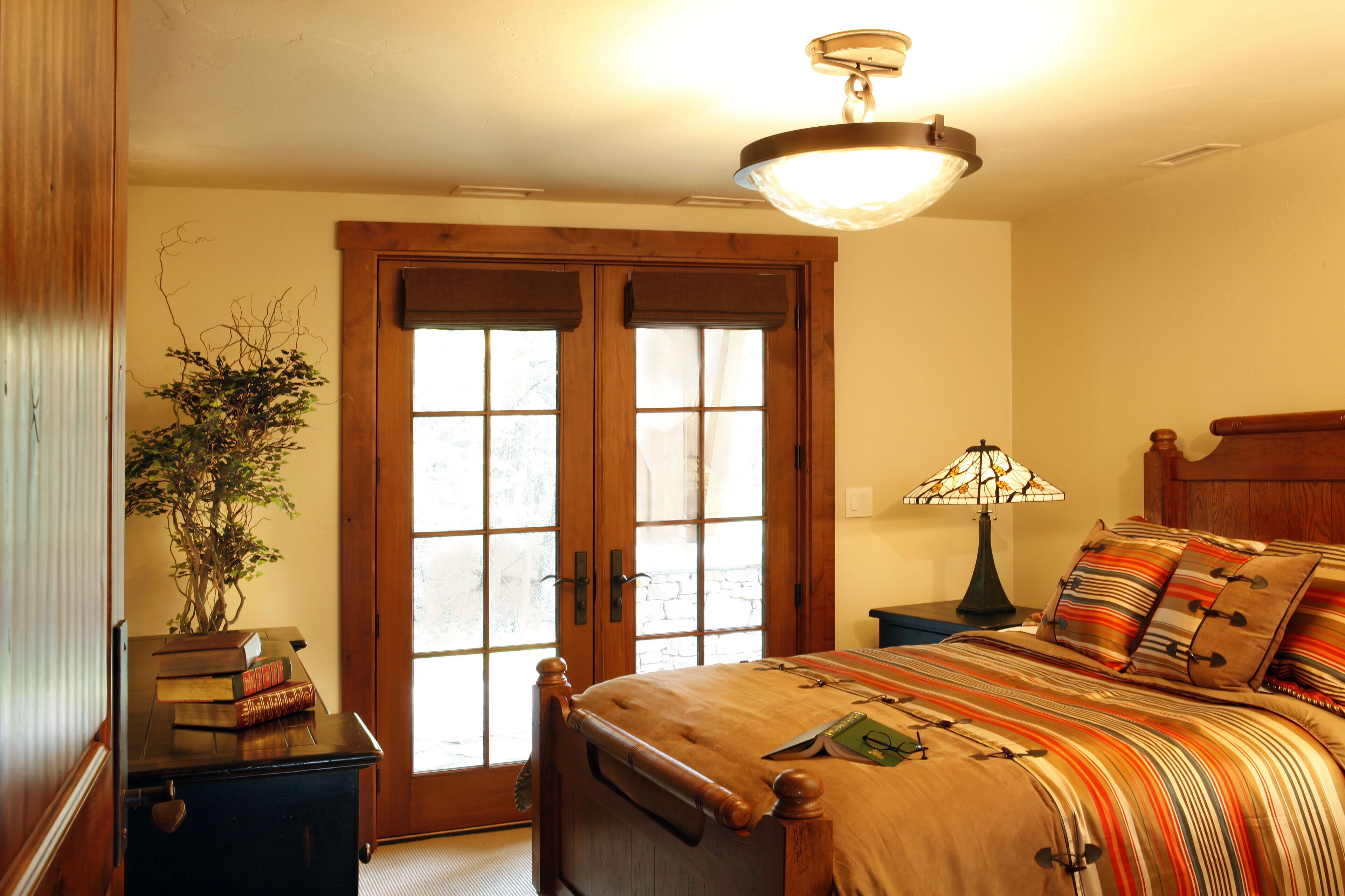 A bedroom with a bed, a nightstand, a lamp, a potted plant, and a door with glass panels.