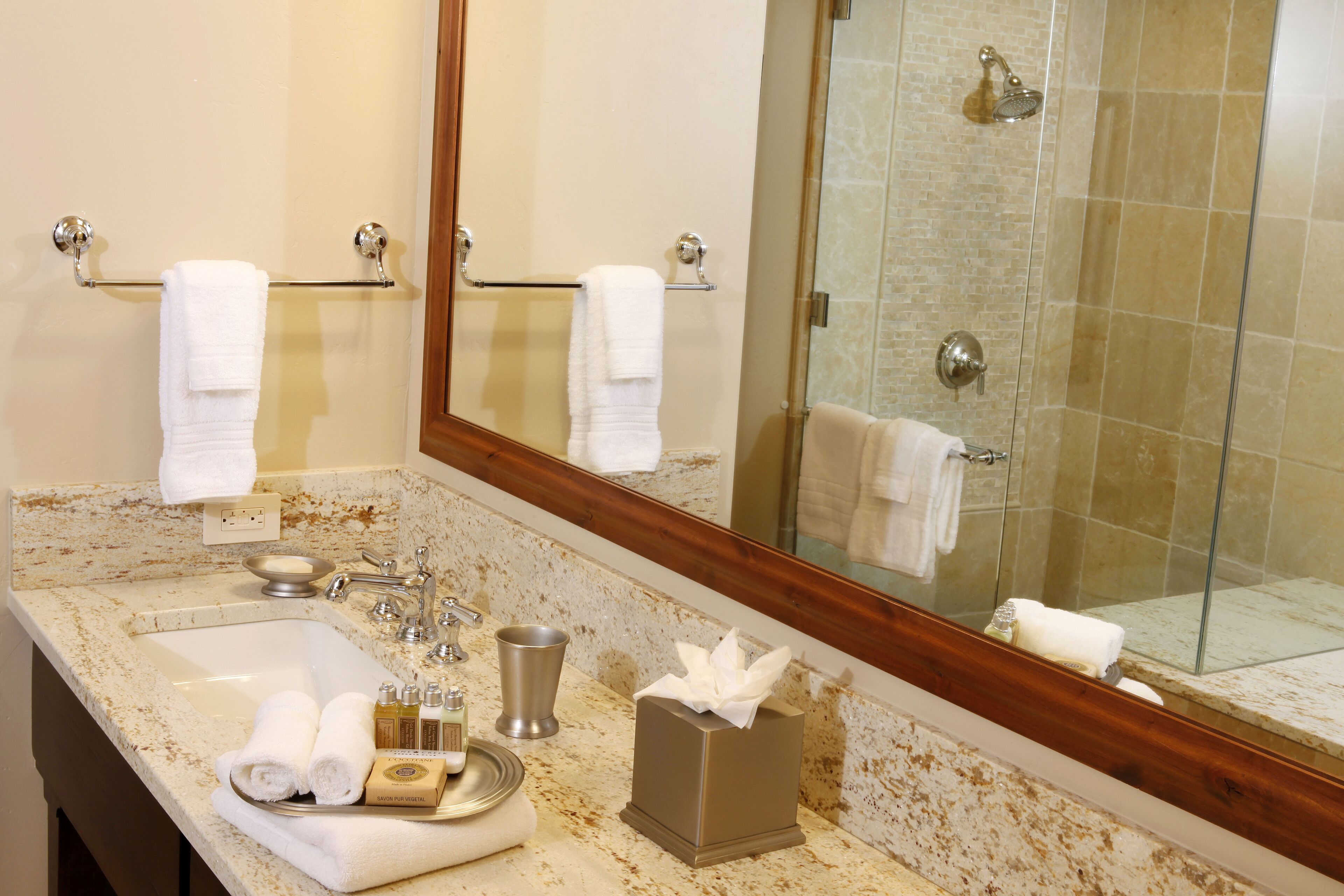 A bathroom with a sink, mirror, and shower. There are towels and toiletries on the counter.