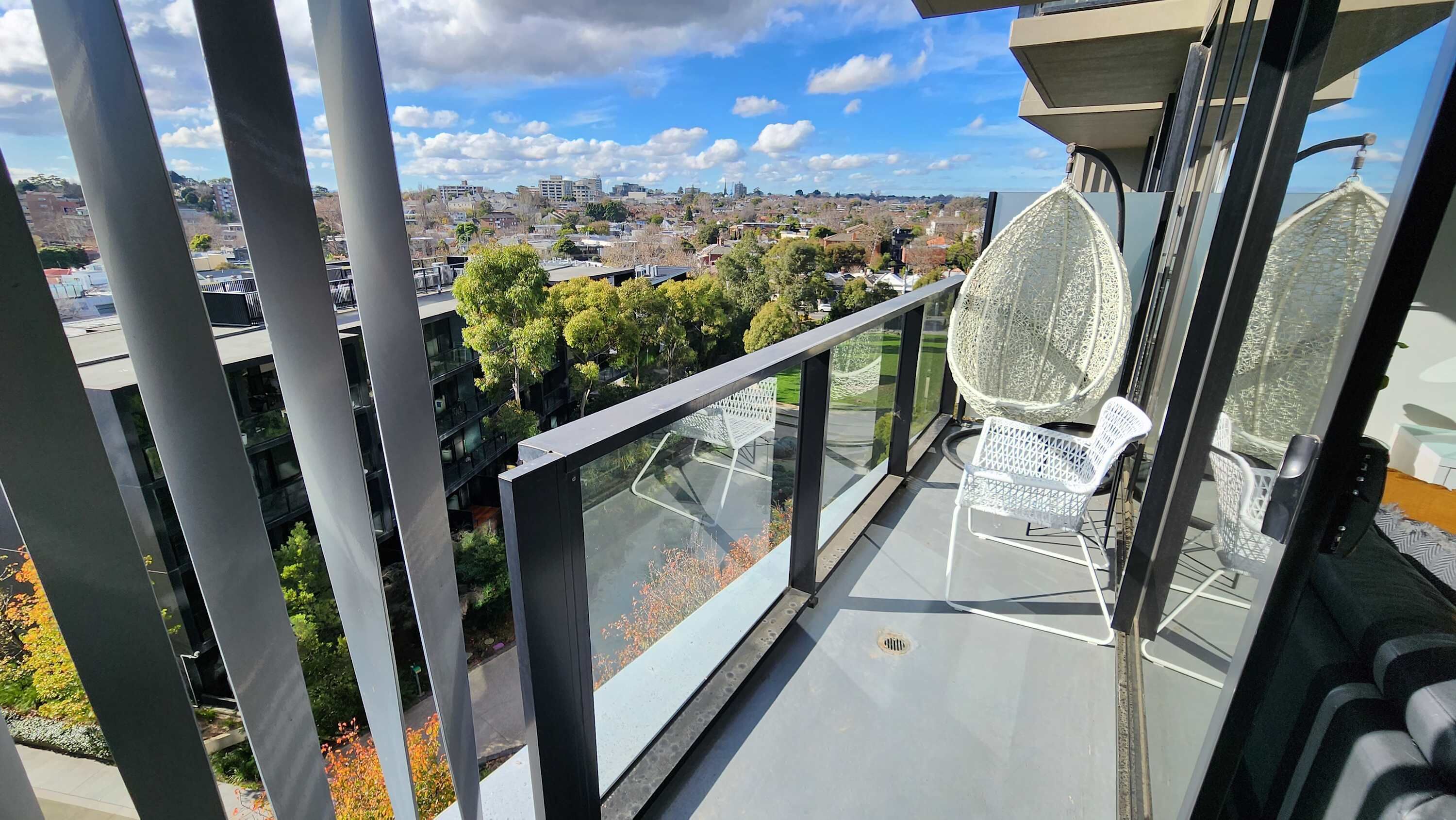 A balcony with a glass railing, a white chair, and a hanging chair.