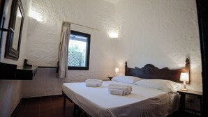 Un dormitorio con una cama grande, dos mesitas de noche con lámparas, un ventanal con cortinas y una pared con textura.