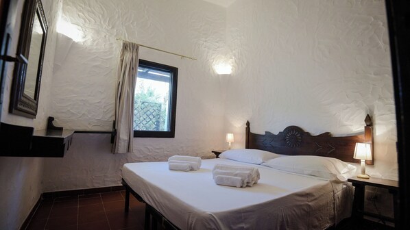 A bedroom with a large bed, two bedside tables with lamps, a window with curtains, and a textured wall.