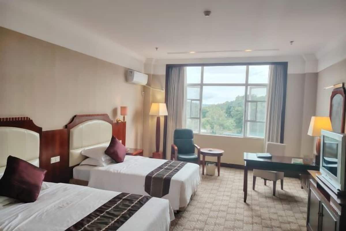 A hotel room with two beds, a desk, a chair, a TV, and a large window with a view.