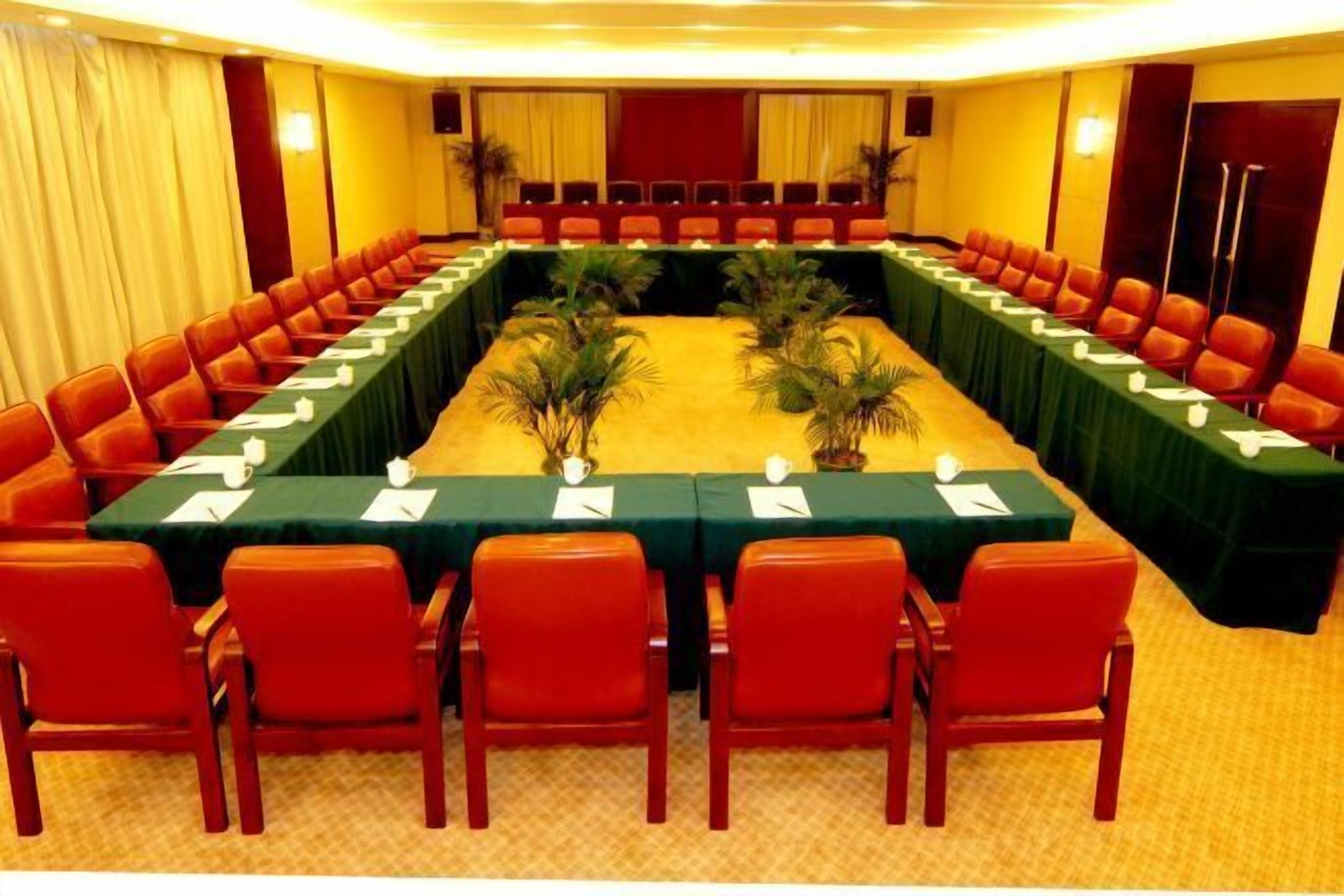Uma sala de conferências com uma mesa comprida, cadeiras vermelhas e toalhas de mesa verdes.